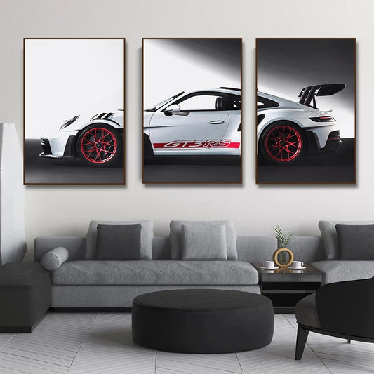 Three framed pictures of a white sports car with red wheels on a wall above a gray sofa.