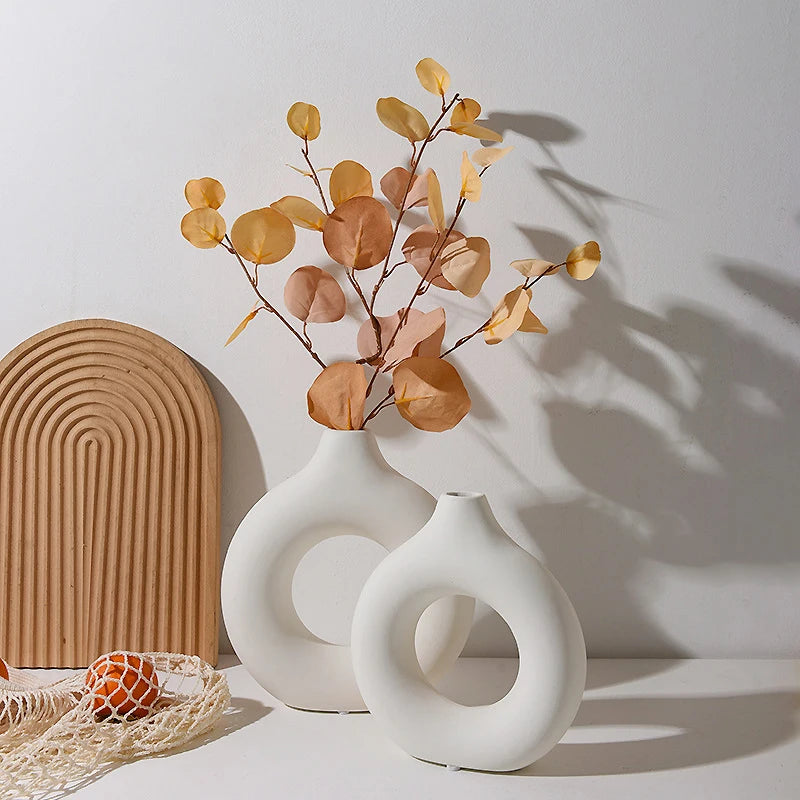 Two white ceramic vases with circular designs on a light surface, featuring a branch with orange leaves.